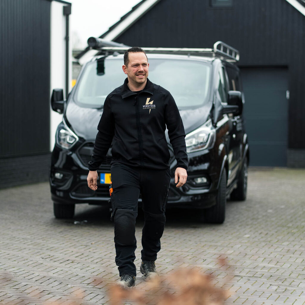 Monteur van Versteeg Elektrotechniek loopt voor servicebus bij woning