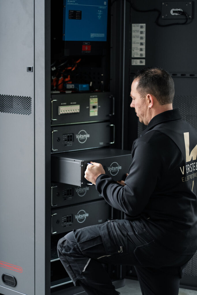 Een elektromonteur van Versteeg Elektrotechniek schuift een modulaire Voltsmile accu-unit in een energieopslagsysteem voor een thuisbatterij.